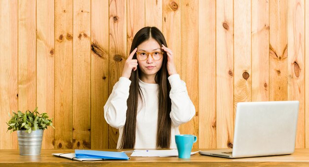 Jonge Chinese vrouw die op haar bureau bestudeert concentreerde zich op een taak, wijsvingers houdend hoofd houdend.