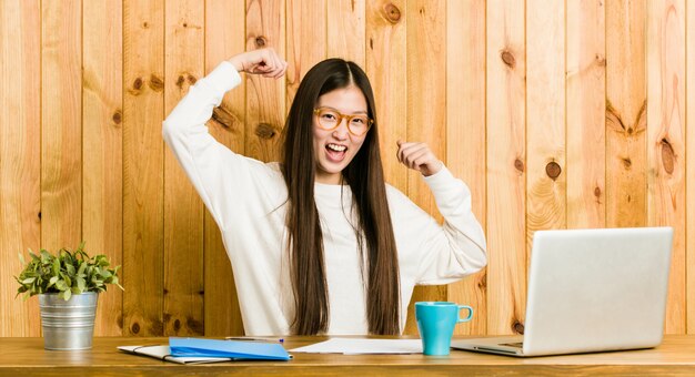 Jonge Chinese vrouw die op haar bureau bestudeert dat een speciale dag viert, sprongen en wapens met energie opheft.