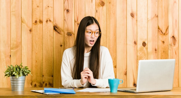 Jonge Chinese vrouw die op haar bureau bestudeert dat wordt geschokt wegens iets dat zij heeft gezien.