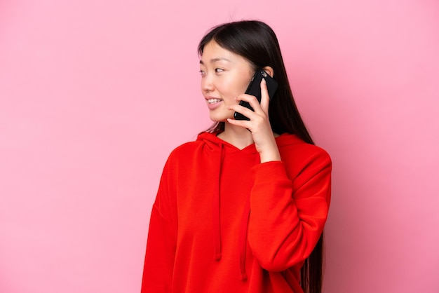 Jonge Chinese vrouw die op roze achtergrond een gesprek met de mobiele telefoon met iemand houdt