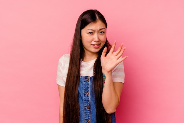 Jonge chinese vrouw die op roze muur wordt geïsoleerd die iemand verwerpt die een gebaar van walging toont.