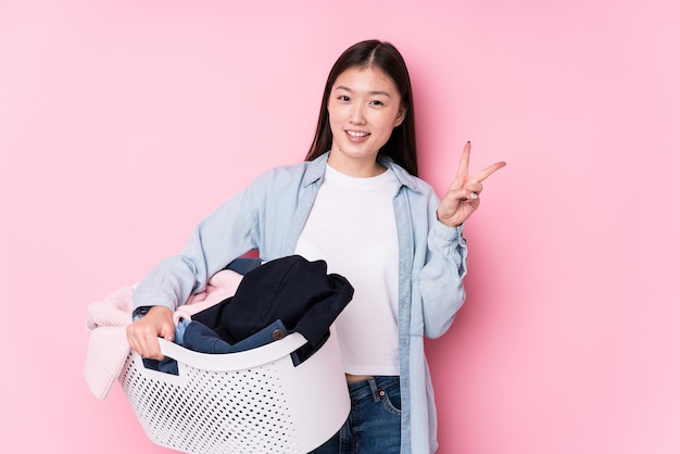 Jonge Chinese vrouw die vuile kleren opnemen blij en onbezorgd tonend een vredessymbool met vingers.