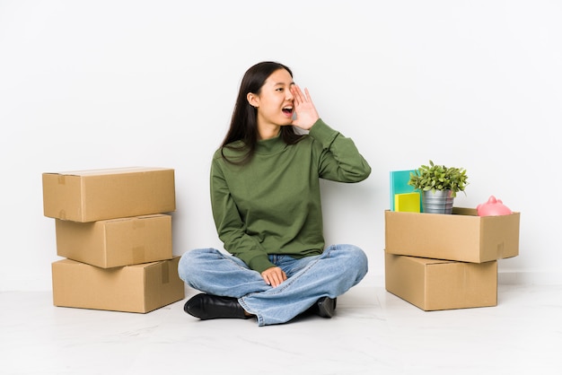 Jonge Chinese vrouw die zich naar een nieuw huis beweegt dat en palm dichtbij geopende mond schreeuwt houdt.