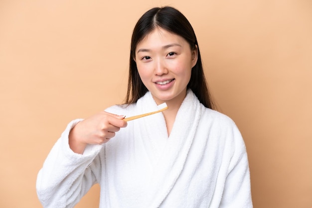 Jonge Chinese vrouw geïsoleerd op beige achtergrond met een tandenborstel en gelukkig expression