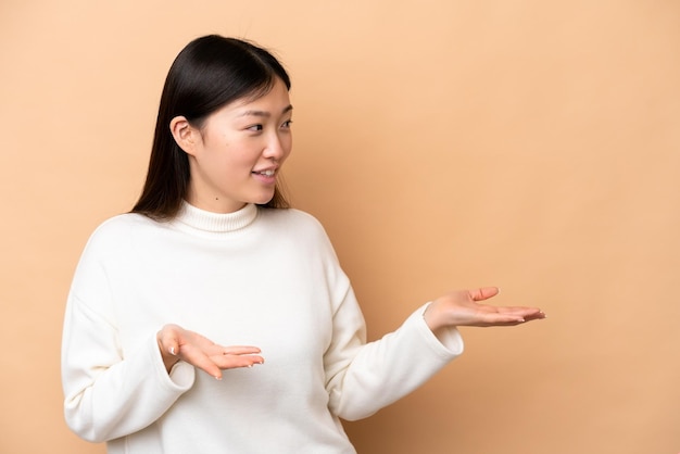 Jonge Chinese vrouw geïsoleerd op beige achtergrond met verrassingsuitdrukking terwijl ze opzij kijkt