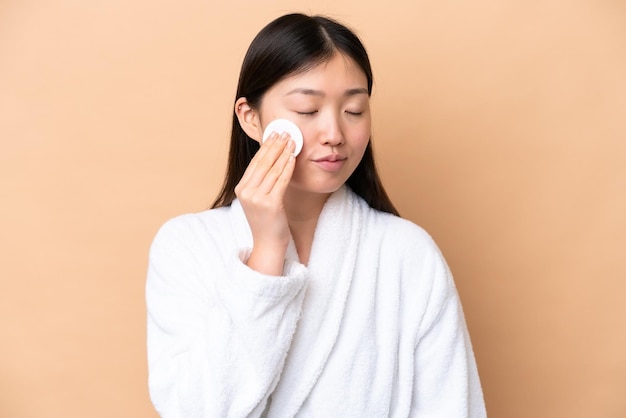 Jonge Chinese vrouw geïsoleerd op beige achtergrond met wattenschijfje voor het verwijderen van make-up van haar gezicht