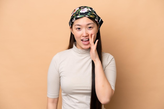 Jonge Chinese vrouw geïsoleerd op beige achtergrond schreeuwen met wijd open mond