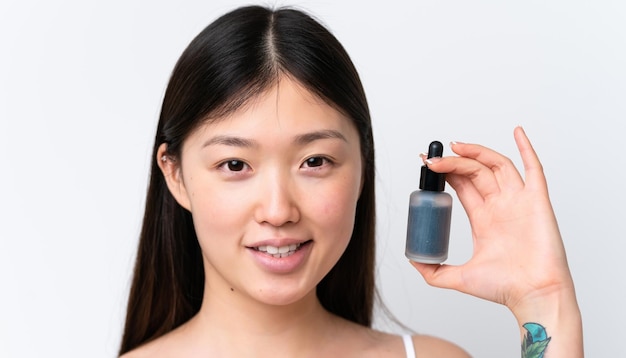 Jonge Chinese vrouw geïsoleerd op een witte achtergrond die een serum vasthoudt terwijl ze lacht Close-up portret