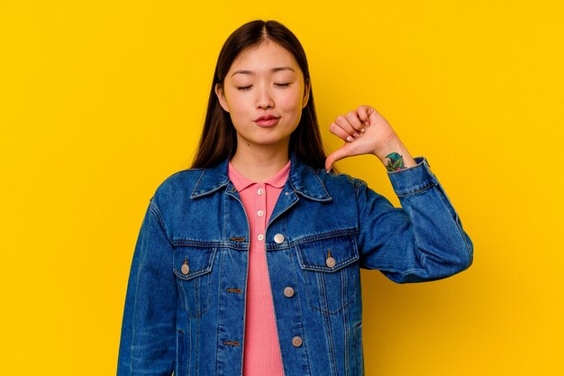 Jonge chinese vrouw geïsoleerd op geel met een afkeer gebaar, duimen naar beneden. Meningsverschil concept.