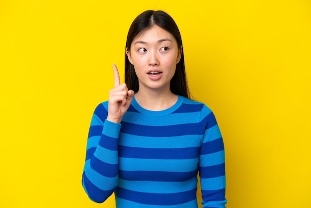 Jonge Chinese vrouw geïsoleerd op gele achtergrond denken een idee met de vinger omhoog