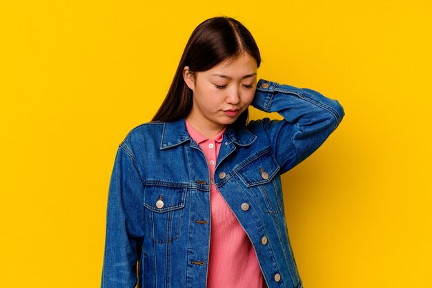 Jonge chinese vrouw geïsoleerd op gele achtergrond met nekpijn als gevolg van stress, masseren en aanraken met de hand.