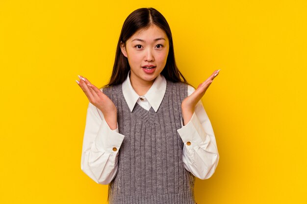 Jonge Chinese vrouw geïsoleerd op gele muur verrast en geschokt