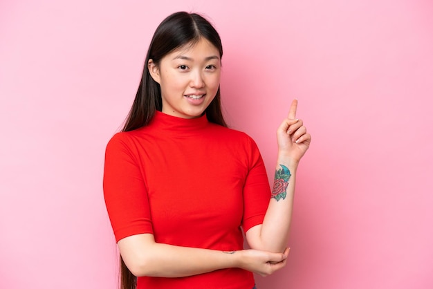 Jonge Chinese vrouw geïsoleerd op roze achtergrond blij en omhoog wijzend