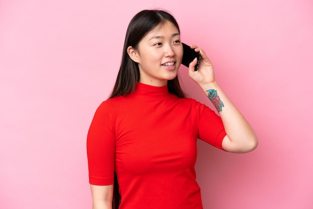Jonge Chinese vrouw geïsoleerd op roze achtergrond die een gesprek voert met de mobiele telefoon
