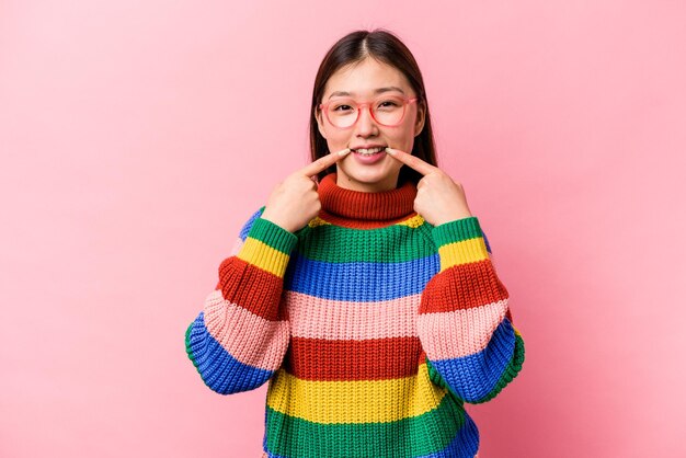 Jonge Chinese vrouw geïsoleerd op roze achtergrond glimlacht wijzende vingers naar mond