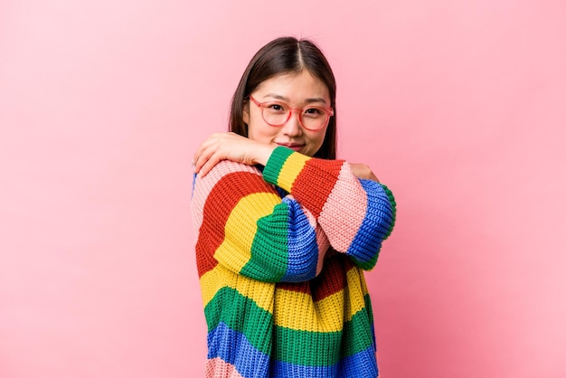 Jonge Chinese vrouw geïsoleerd op roze achtergrond knuffels glimlachend zorgeloos en gelukkig