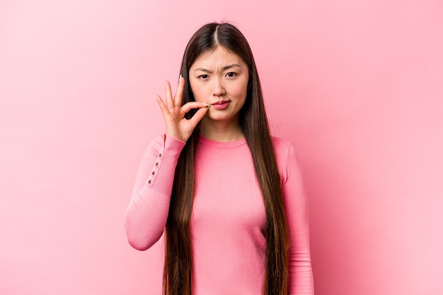 Jonge Chinese vrouw geïsoleerd op roze achtergrond met vingers op lippen die een geheim houden