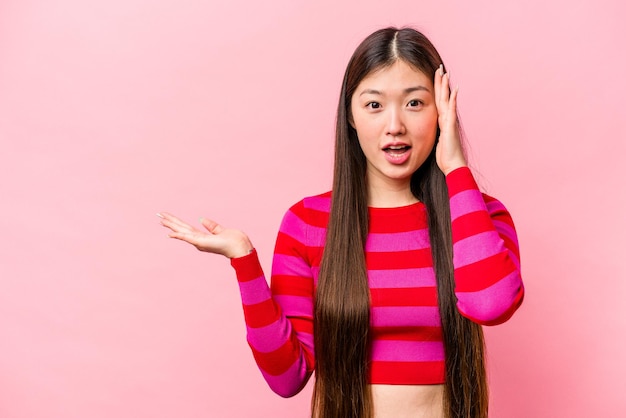Jonge Chinese vrouw geïsoleerd op roze achtergrond onder de indruk met kopie ruimte op palm