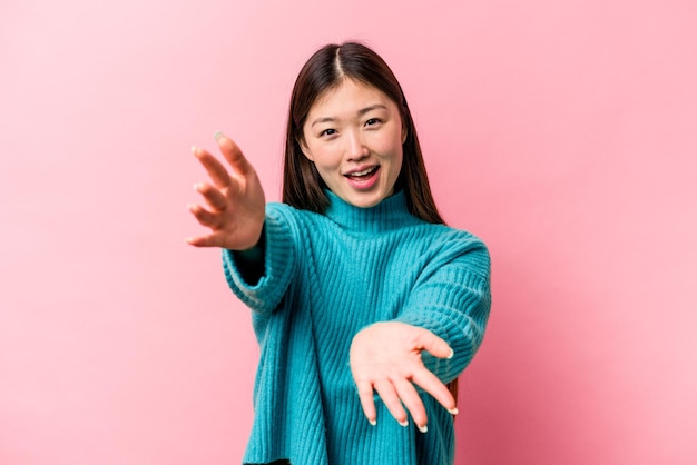 Jonge Chinese vrouw geïsoleerd op roze achtergrond voelt zich zelfverzekerd en geeft een knuffel aan de camera