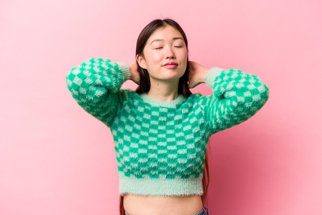 Jonge Chinese vrouw geïsoleerd op roze achtergrond voelt zich zelfverzekerd met handen achter het hoofd