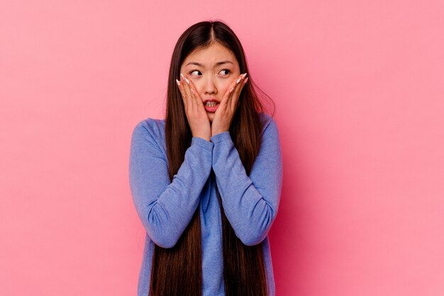 Jonge chinese vrouw geïsoleerd op roze muur bang en bang.