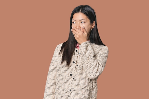 Jonge Chinese vrouw in een studio die bedachtzaam naar een kopieringsruimte kijkt en haar mond met haar hand bedekt