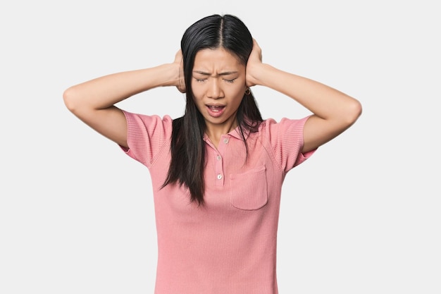 Jonge Chinese vrouw in een studio die haar oren met haar handen bedekt probeert te luid geluid niet te horen