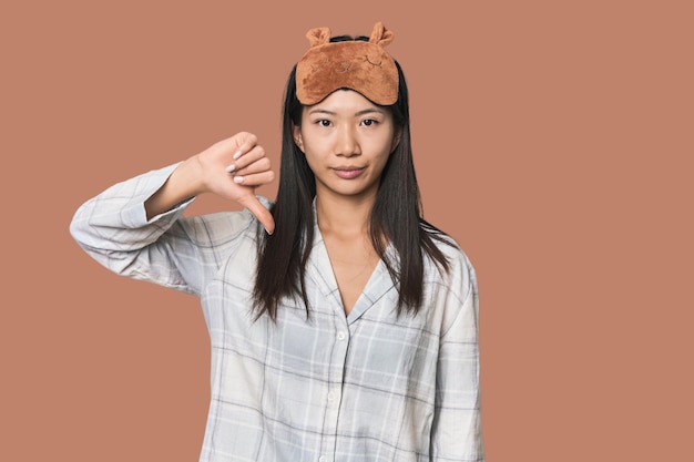 Jonge Chinese vrouw in pyjama masker toont een afkeer gebaar duimen naar beneden meningsverschil concept