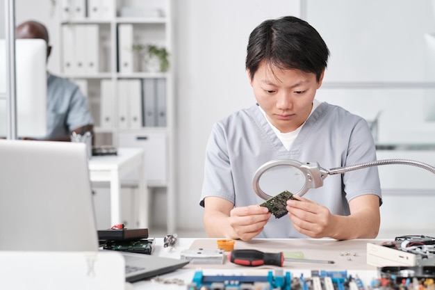 Jonge Chinese vrouw in uniform kijkt naar microchip in bord