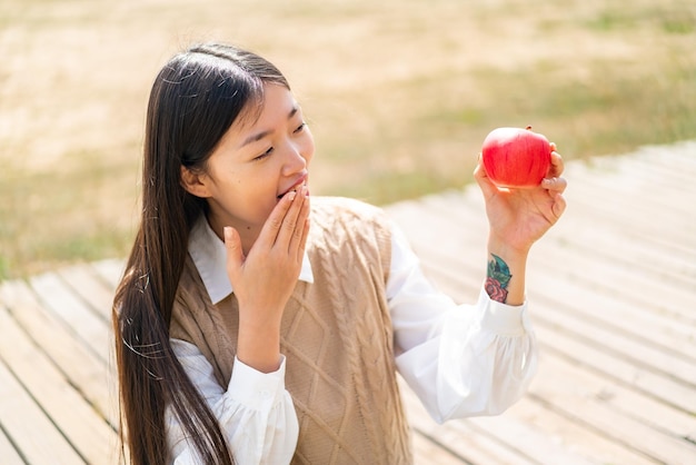 Jonge Chinese vrouw met een appel in de open lucht met verrassing en geschokte gezichtsuitdrukking