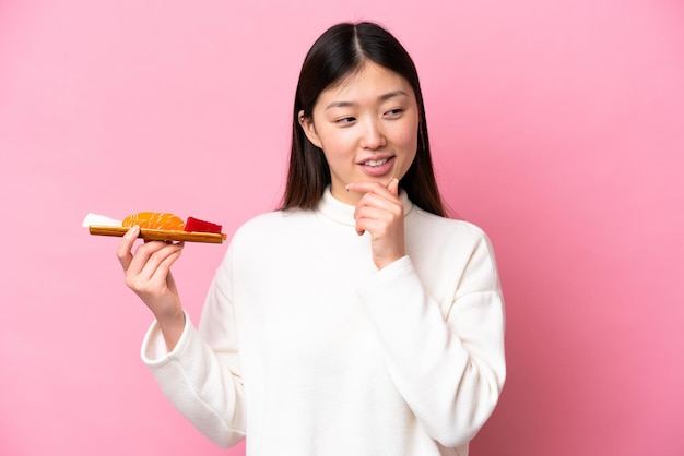 Jonge Chinese vrouw met sashimi geïsoleerd op roze achtergrond kijkend naar de zijkant en glimlachend