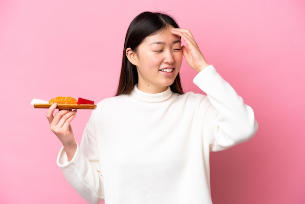 Jonge Chinese vrouw met sashimi geïsoleerd op roze achtergrond lacht veel