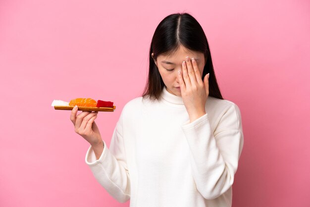 Jonge Chinese vrouw met sashimi geïsoleerd op roze achtergrond met vermoeide en zieke uitdrukking