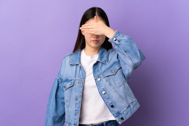 Jonge Chinese vrouw over geïsoleerde paarse muurbedekking ogen door handen. Ik wil niets zien