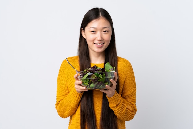 Jonge Chinese vrouw over geïsoleerde witte muur die een kom salade met gelukkige uitdrukking houdt