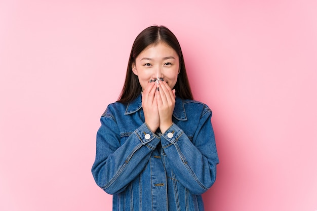 Jonge chinese vrouw poseren in een roze oppervlak geïsoleerd lachen om iets, mond bedekken met handen.