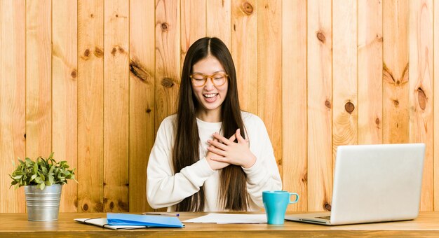 Jonge chinese vrouw studeren op haar bureau lachen houden handen op hart, concept van geluk.
