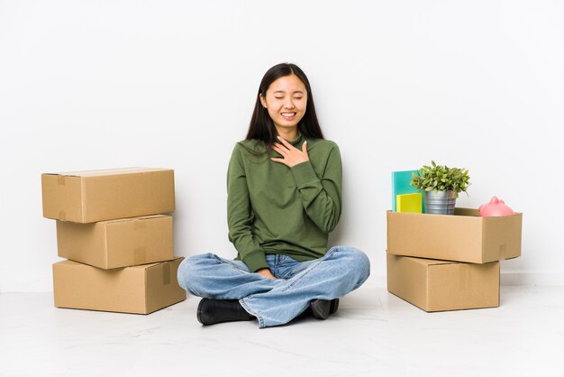 Jonge chinese vrouw verhuizen naar een nieuw huis lacht hardop hand op de borst te houden.