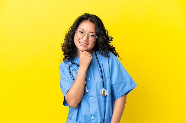 Jonge chirurg arts Aziatische vrouw geïsoleerd op gele achtergrond met een bril en lachend