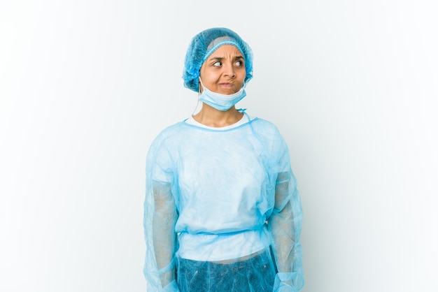 Jonge chirurg Latijnse vrouw die op wit wordt geïsoleerd verward, twijfelachtig en onzeker voelt.