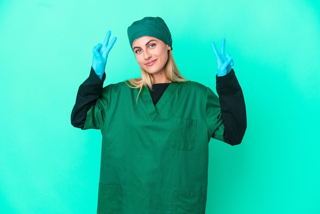 Jonge chirurg Uruguayaanse vrouw in groen uniform geïsoleerd op blauwe achtergrond met overwinningsteken met beide handen