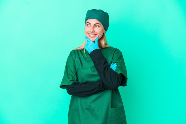 Jonge chirurg Uruguayaanse vrouw in groen uniform geïsoleerd op blauwe achtergrond op zoek naar de zijkant