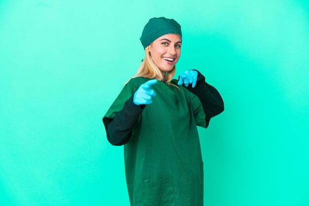 Jonge chirurg Uruguayaanse vrouw in groen uniform geïsoleerd op blauwe achtergrond, wijzend naar voren en glimlachend