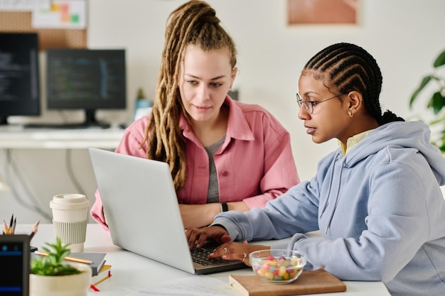 Jonge collega's ontwikkelen nieuwe software in team ze zitten aan tafel en werken op laptop