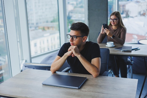 Jonge collega's op kantoor op de desktop met een laptop Jonge moderne collega's in slimme vrijetijdskleding werken terwijl ze op kantoor werken