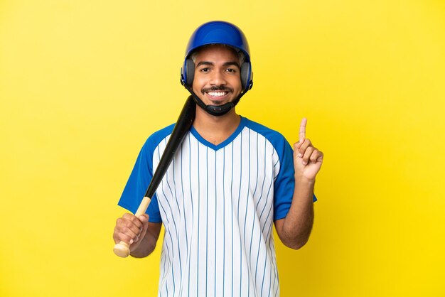 Jonge Colombiaanse Latijns-man die honkbal speelt geïsoleerd op een gele achtergrond die een vinger toont en optilt in teken van de beste