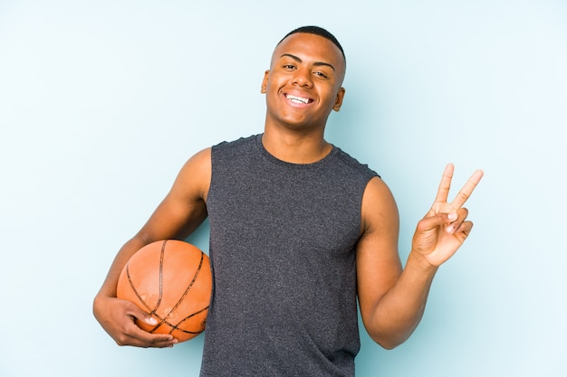 Jonge Colombiaanse man met basketbal geïsoleerd vrolijk en zorgeloos met een vredessymbool met vingers.