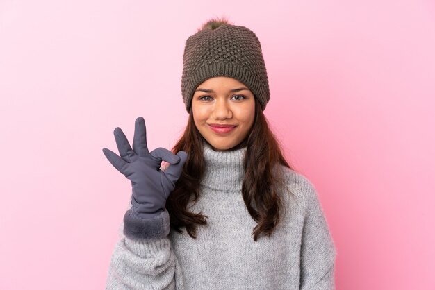 Foto jonge colombiaanse vrouw met winter hoed over geïsoleerde roze muur met een ok bord met vingers