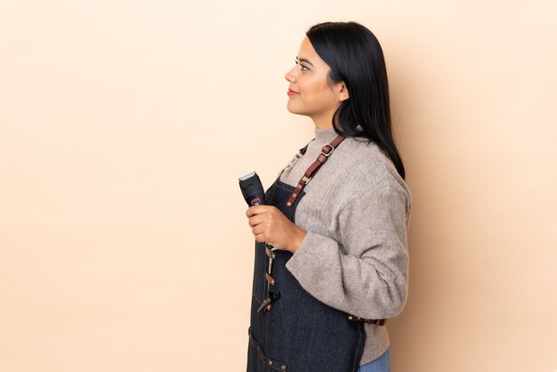 Jonge Colombiaanse vrouwenkapper die op beige muur wordt geïsoleerd die aan de kant kijkt