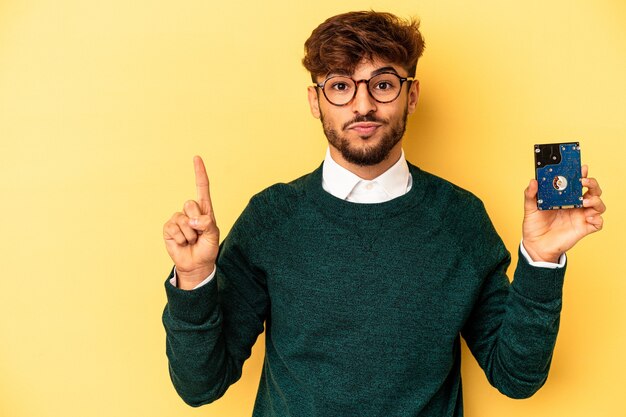 Jonge computerizer man geïsoleerd op gele achtergrond met nummer één met vinger.